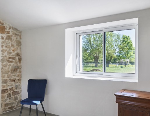 Intérieur de maison aux murs blancs avec vue sur la verdure depuis une fenêtre coulissante | Menuiseries Bouvet